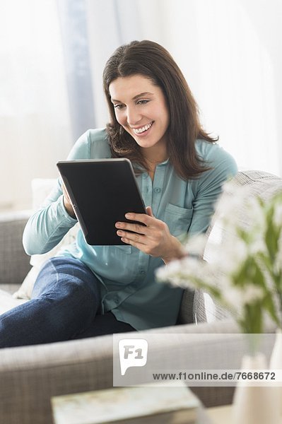 Woman using digital tablet while sitting on sofa