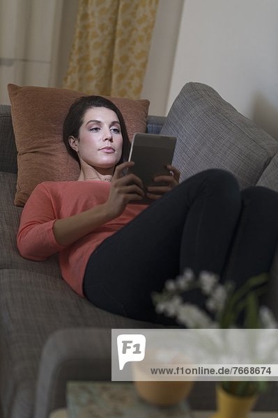 Woman using digital tablet while lying on sofa