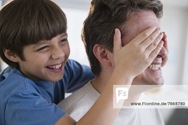 Son (8-9) covering father's eyes