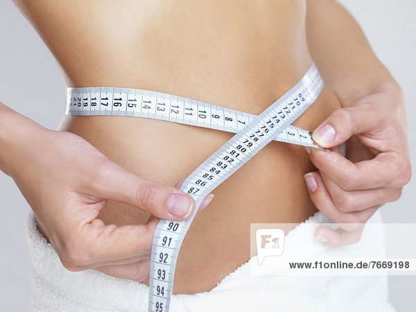 Studio Shot  Woman measuring her waist with tape measure