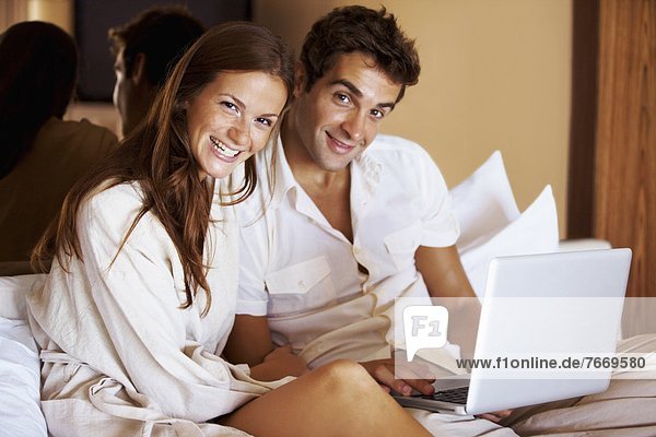 Couple using laptop while sitting on bed