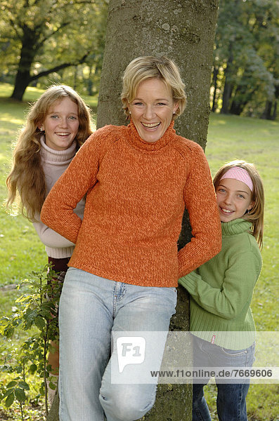 Mother and two daughters standing around a tree in a park