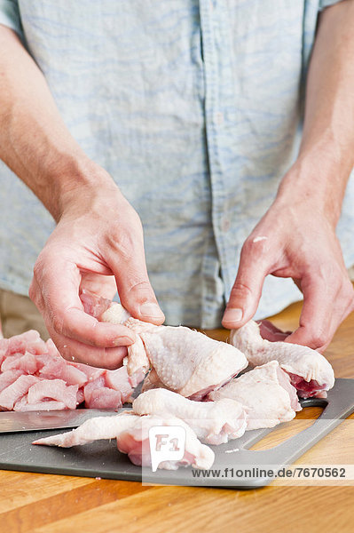 Man handling pieces of uncooked chicken in a kitchen