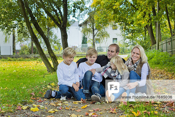 Family with three children sitting on a meadow with autumn leaves
