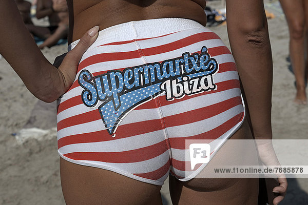 'Weibliches Mitglied eines Promotion-Teams von einem der großen Clubs wirbt mit Aufschrift für den Club ''Supermartxé'' auf ihrem Bikini-Unterteil  vor dem Sa Trinxa-Beachlokal  Platja de Ses Salines  Ibiza  Pityusen  Balearen  Spanien  Europa'