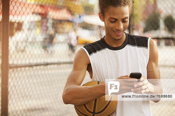 Mann mit Handy auf dem Basketballplatz
