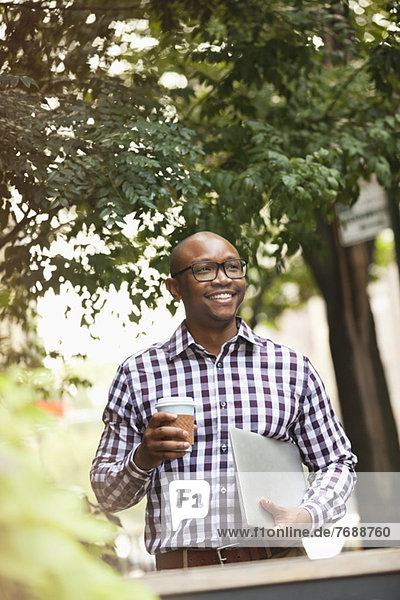 Mann mit Kaffee und Laptop auf der Straße in der Stadt