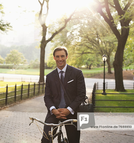 Businessman sitting on bicycle in urban park