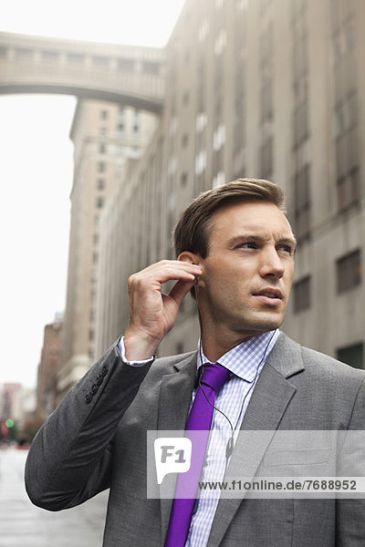 Businessman listening to earphones on city street