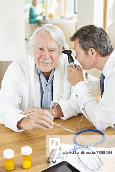 Arzt untersucht das Ohr des älteren Mannes bei Hausbesuch