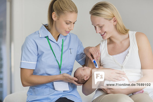 Mutter und Krankenschwester messen die Temperatur des Neugeborenen