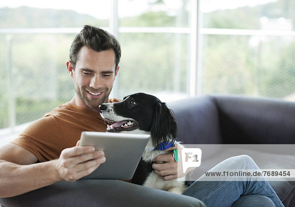 Mann streichelt Hund und benutzt Tablet-Computer