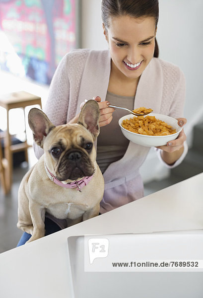 Frau isst Müsli mit Hund auf dem Schoß
