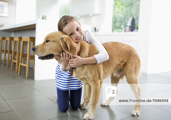 Lächelndes Mädchen umarmt Hund in der Küche