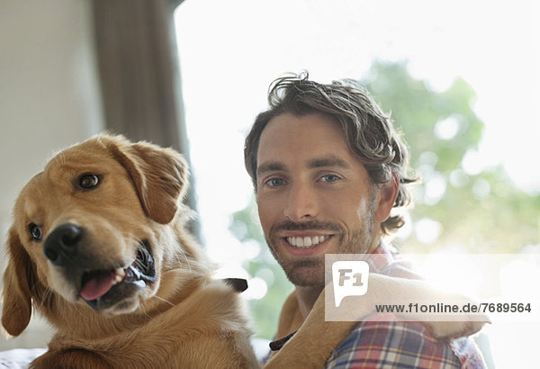 Lächelnder Mann streichelt Hund im Haus