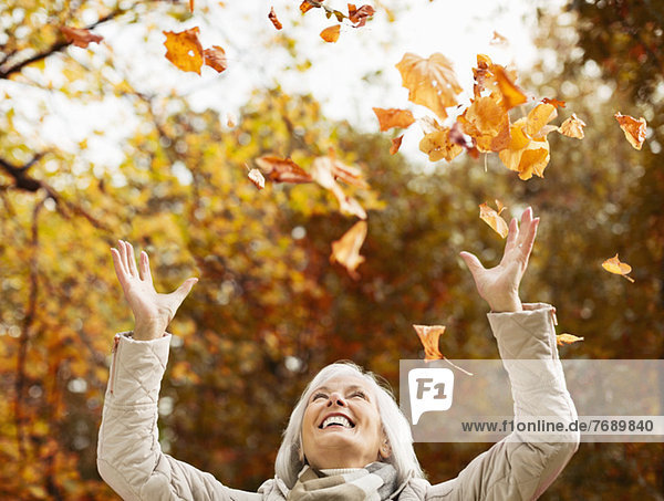 Older woman playing in autumn leaves