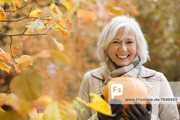 Older woman holding pumpkin in park
