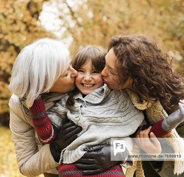 Woman and daughter kissing girl in park