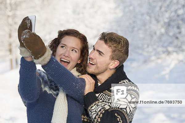 Caucasian couple taking pictures in snow