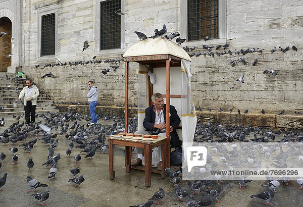 Mann verkauft Vogelfutter  umgeben von Tauben  vor Yeni Cami oder Neue Moschee