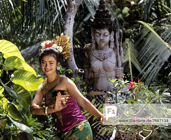 Balinese dancer wearing a traditional costume in front of a stone statue