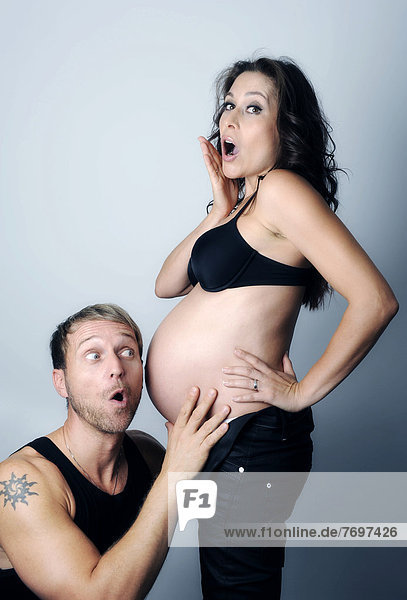 Mann lauscht am Schwangerschaftsbauch seiner Frau  beide mit erstauntem Blick