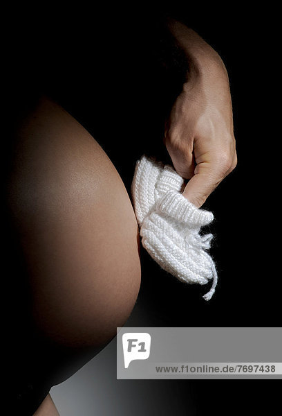 Hand lässt weiße Babyschuhe über einen Schwangerschaftsbauch laufen