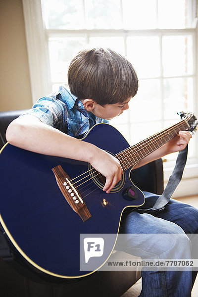 Junge spielt Gitarre auf Sofa