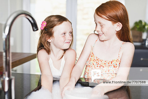 Lächelnde Mädchen beim Geschirrspülen im Waschbecken