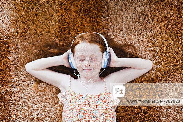 Mädchen hört Kopfhörer auf dem Teppich