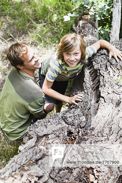 Father helping son over fallen tree