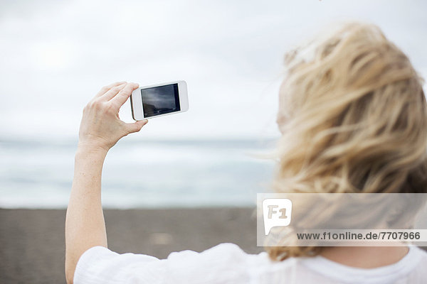 Frau macht Handyfoto am Strand