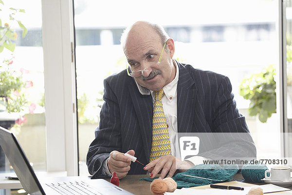 Geschäftsmann lackiert seine Nägel am Schreibtisch