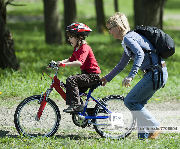 Mother pushing son on bicycle in park