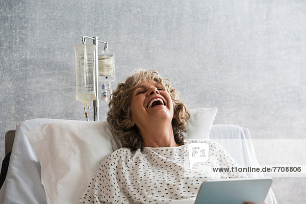 Female hospital patient with digital tablet  laughing