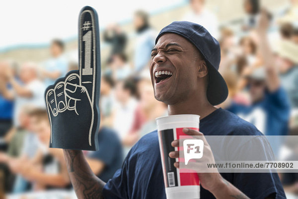 Man at sports game with foam hand and soft drink cup