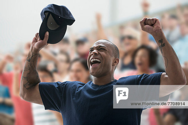 Man cheering at sports game  holding baseball cap