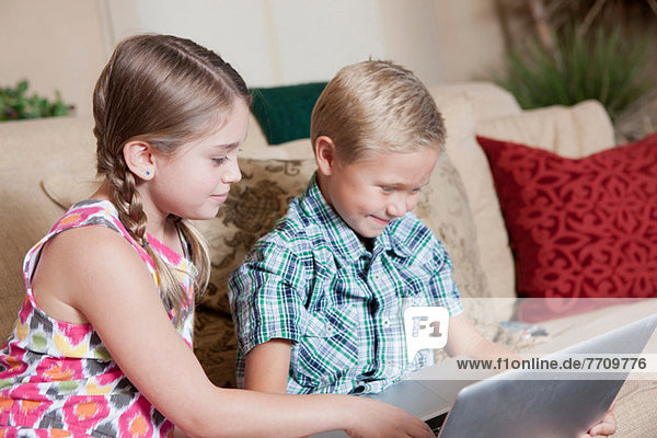 Kinder  die den Laptop gemeinsam auf dem Sofa benutzen