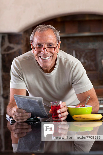 Älterer Mann beim Zeitungslesen beim Frühstück