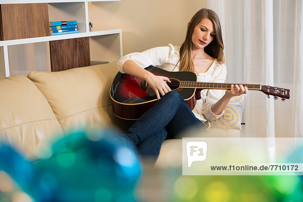 Frau spielt Gitarre auf dem Sofa