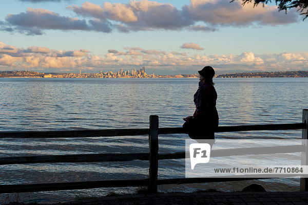 Silhouette of woman sitting on fence