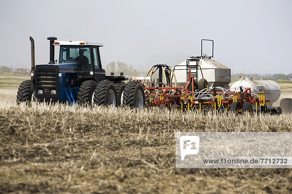Tractor With Air Seeder And Ammonia Tank In Stubble Field With Hazy Blue Sky  Alberta  Canada