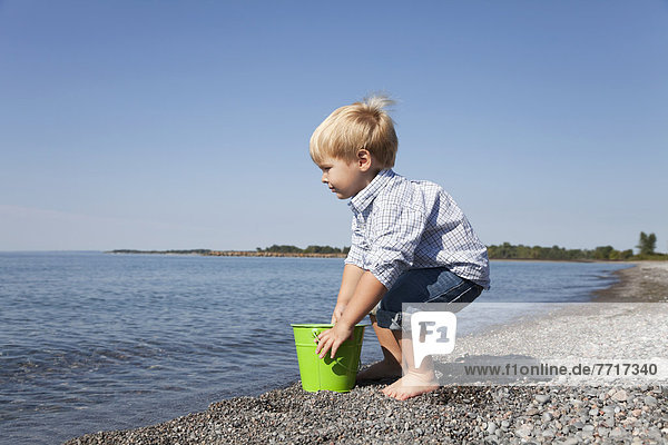 Young boy playing with a pail on the beach by lake ontario Ontario canada