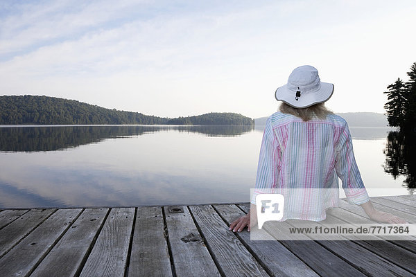 Senior woman sitting on her cottage dock looking out at lake in algonquin park Ontario canada