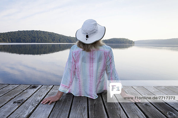 Senior woman sitting on her cottage dock looking out at lake in algonquin park Ontario canada
