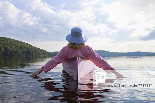 Senior woman dressed in pink and trailing her hands in the water from her pink canoe in algonquin park Ontario canada