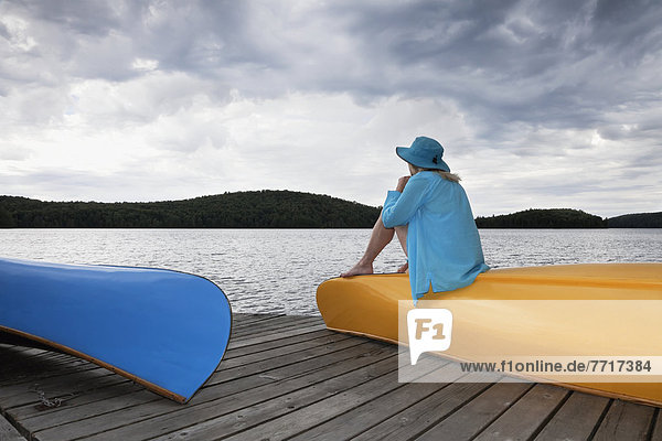 Senior woman sitting on her yellow canoe and looking up at a stormy sky in algonquin park Ontario canada