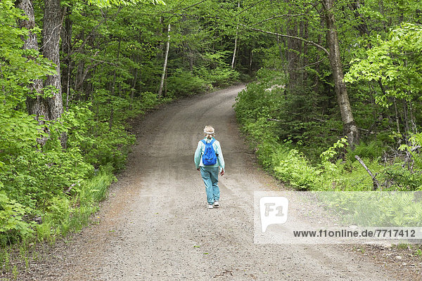 Senior woman walking down a tree-lined dirt road in algonquin park in spring Ontario canada