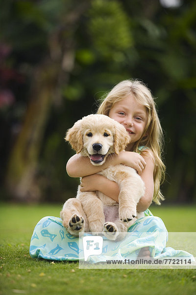 Hawaii  Maui  Little Girl Sits On Grass Holding A Golden Retriever Puppy.