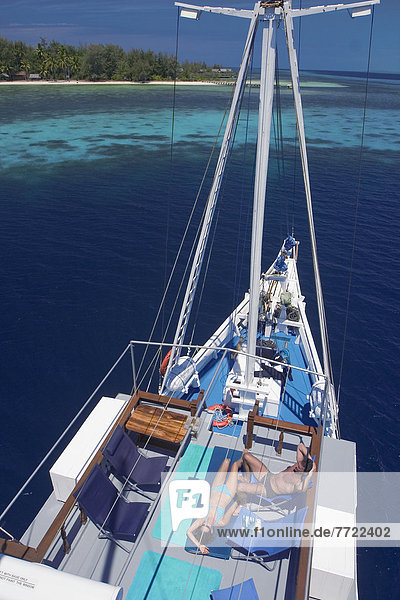 Indonesia  Raja Ampat Islands  Couple Sunbathes On Deck Of Live-Aboard Dive Boat.